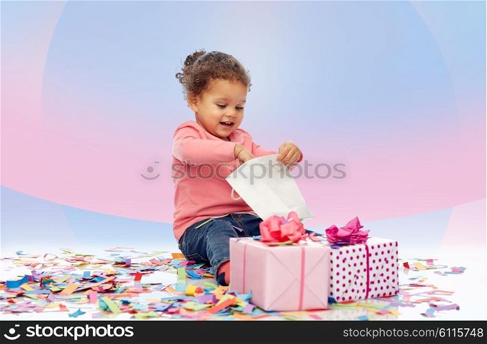 childhood, birthday, party, holidays and people concept - happy smiling little african american baby girl with gift boxes playing with shopping bag and sitting on floor over pink violet background