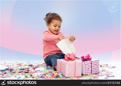 childhood, birthday, party, holidays and people concept - happy smiling little african american baby girl with gift boxes playing with shopping bag and sitting on floor over pink violet background