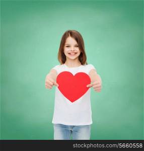childhood, cahrity, education, love and people concept - smiling little girl sitting with red heart cutout over green blackboard background