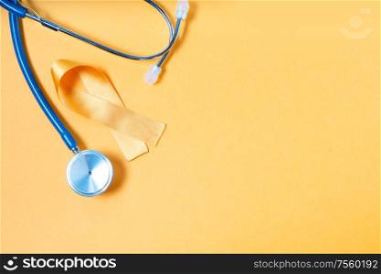 Childhood Cancer Awareness yellow ribbon and stethoscope on yellow background with copy space, top view. Childhood Cancer Awareness concept