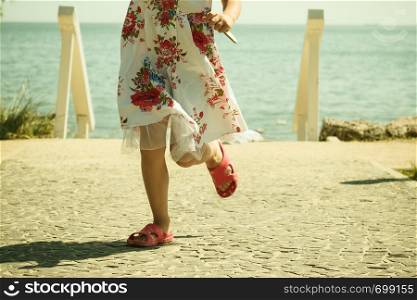 Childhood carefree concept. Little girl wearing dress running outside, sea water in background, photo of legs.. Little girl wearing dress running outside