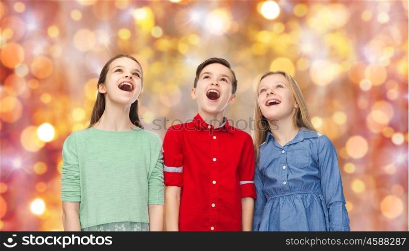 childhood, charistmas, holidays, party and people concept - happy amazed boy and girls looking up with open mouths over lights background