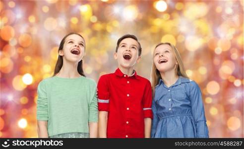 childhood, charistmas, holidays, party and people concept - happy amazed boy and girls looking up with open mouths over lights background