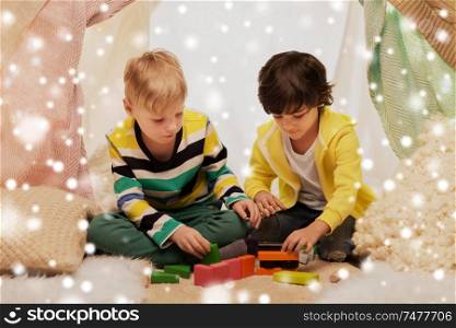 childhood, christmas and friendship concept - happy boys playing toy blocks in kids tent or teepee at home over snow. boys playing toy blocks in kids tent at home