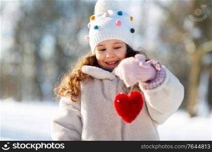 childhood, christmas and valentine&rsquo;s day concept - portrait of happy little girl in winter clothes holding toy heart outdoors at park. happy little girl with heart outdoors in winter