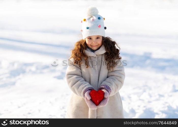 childhood, christmas and valentine&rsquo;s day concept - portrait of happy little girl in winter clothes holding toy heart outdoors at park. happy little girl with heart outdoors in winter