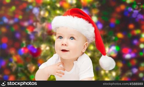 childhood, christmas, holidays and people concept - beautiful little baby boy in christmas santa hat over lights background