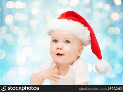 childhood, christmas, holidays and people concept - beautiful little baby boy in christmas santa hat over blue lights background