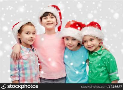 childhood, christmas, winter holidays, friendship and people concept - group of happy smiling little children in santa hats hugging over snow