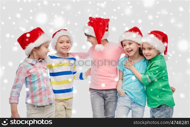 childhood, christmas, winter holidays, friendship and people concept - group of happy smiling little children in santa hats hugging over snow. happy little children in santa hats hugging