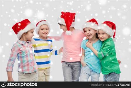childhood, christmas, winter holidays, friendship and people concept - group of happy smiling little children in santa hats hugging over snow. happy little children in santa hats hugging