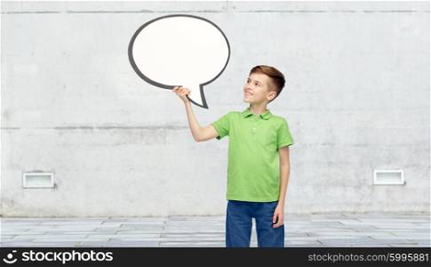 childhood, communication, advertisement and people concept - happy smiling boy in green polo t-shirt holding blank white text bubble banner over urban street background