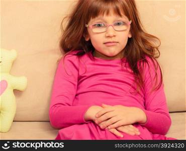 childhood concept. Sad thoughtful little girl in glasses sitting on sofa at home with teddy bear toy