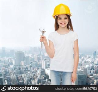 childhood, construction and people concept - smiling little girl in protective helmet with wrench