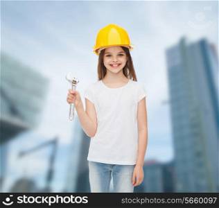 childhood, construction and people concept - smiling little girl in protective helmet with wrench
