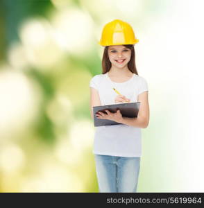 childhood, construction, architecture, building and people concept - smiling little girl in protective helmet with clipboard making notes