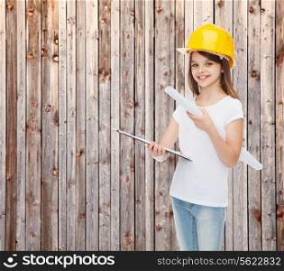 childhood, construction, architecture, building and people concept - smiling little girl in protective helmet with clipboard and blueprint