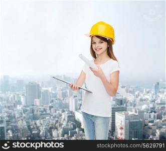 childhood, construction, architecture, building and people concept - smiling little girl in protective helmet with clipboard and blueprint