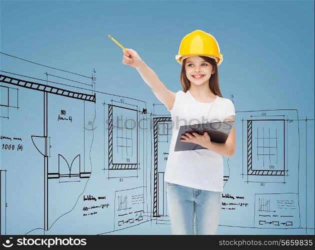 childhood, construction, architecture, building and people concept - smiling little girl in protective helmet with clipboard pointing pencil