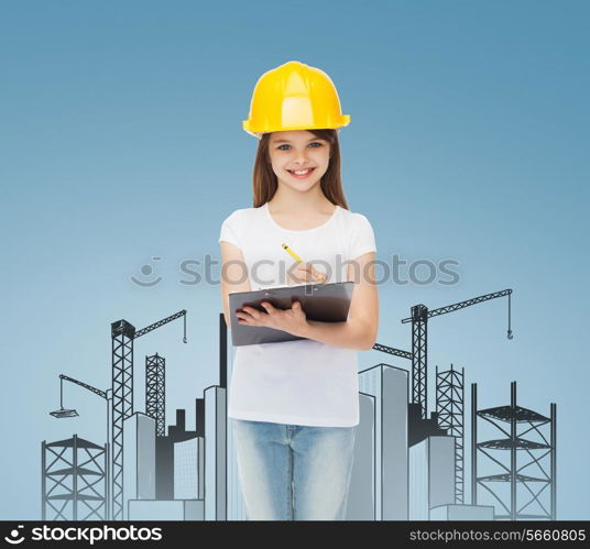 childhood, construction, architecture, building and people concept - smiling little girl in protective helmet with clipboard making notes