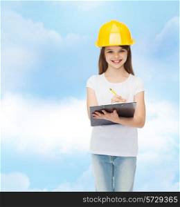 childhood, construction, architecture, building and people concept - smiling little girl in protective helmet with clipboard making notes