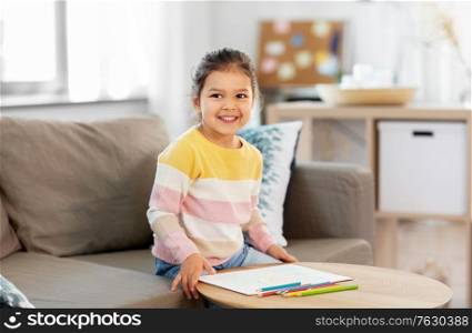 childhood, creativity and art concept - happy smiling little girl drawing with coloring pencils at home. little girl drawing with coloring pencils at home
