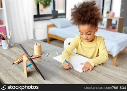 childhood, creativity and art concept - little african american girl with coloring pencils drawing picture on paper at home. little girl drawing with coloring pencils at home