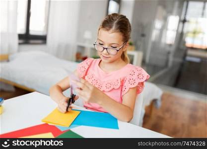 childhood, creativity and hobby concept - creative girl cutting color paper with scissors at home. girl cutting color paper with scissors at home
