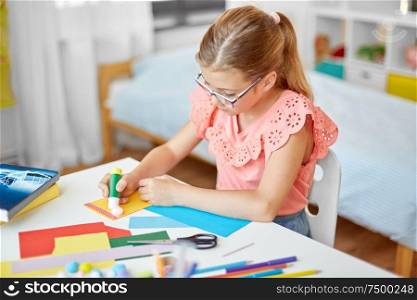 childhood, creativity and hobby concept - creative girl making greeting card and sticking pompon with glue stick at home. creative girl making greeting card at home