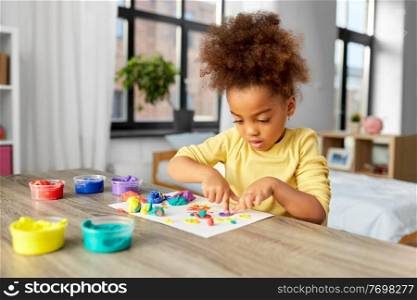 childhood, creativity and hobby concept - little african american girl with modeling clay playing at home. little girl with modeling clay playing at home