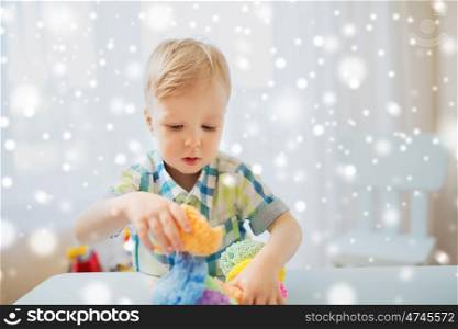 childhood, creativity, arts, activity and people concept - happy little baby boy playing with ball clay at home over snow