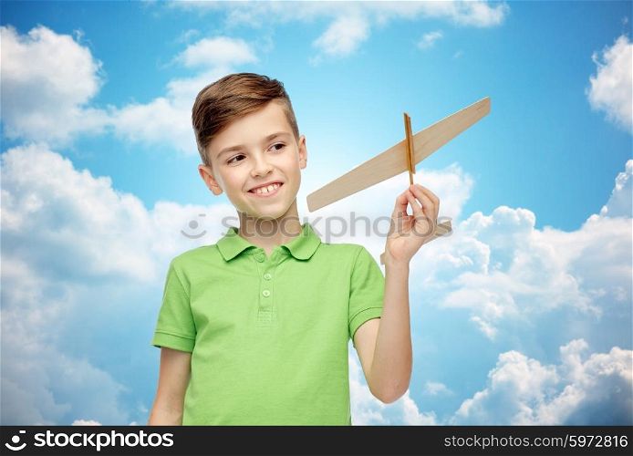 childhood, dream and people concept - happy smiling boy in green polo t-shirt with toy airplane over blue sky and clouds background