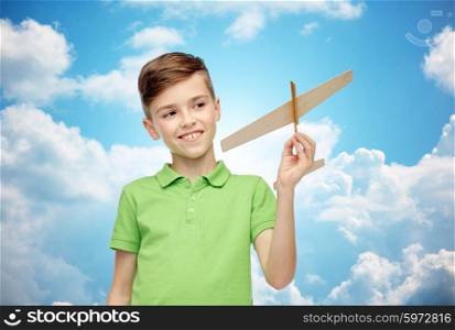 childhood, dream and people concept - happy smiling boy in green polo t-shirt with toy airplane over blue sky and clouds background