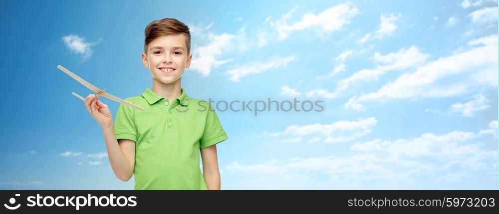 childhood, dream, future and people concept - happy smiling boy in green polo t-shirt with toy airplane over blue sky and clouds background
