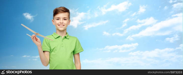 childhood, dream, future and people concept - happy smiling boy in green polo t-shirt with toy airplane over blue sky and clouds background