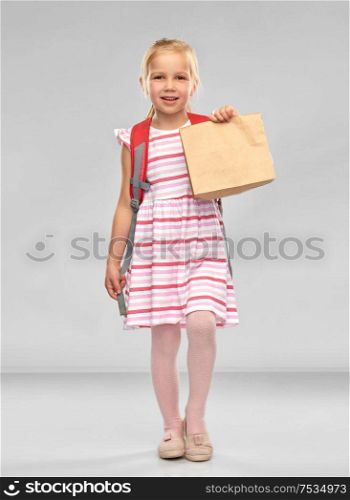 childhood, education and food concept - little student girl with school lunch in paper bag over grey background. little student girl with school lunch in paper bag