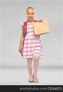 childhood, education and food concept - little student girl with school lunch in paper bag over grey background. little student girl with school lunch in paper bag