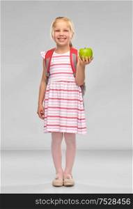 childhood, education and knowledge concept - little student girl with school bag and green apple over grey background. little school girl with green apple