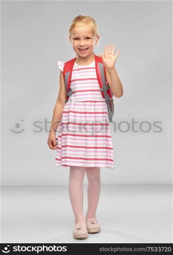 childhood, education and people concept - happy student girl with school bag waving hand over grey background. happy student girl with school bag waving hand