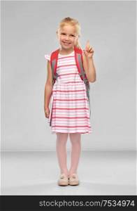 childhood, education and people concept - happy student girl with school bag pointing finger up over grey background. little girl with school bag pointing finger up
