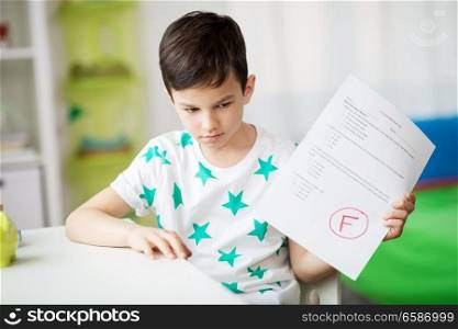 childhood, education and people concept - sad boy holding school test with f grade. sad boy holding school test with f grade