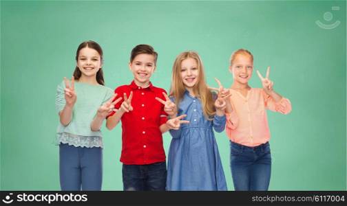 childhood, education, friendship and people concept - happy smiling boy and girls showing peace hand sign over green school chalk board background
