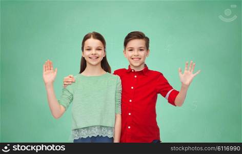 childhood, education, friendship, gesture and people concept - happy smiling boy and girl hugging and waving hand over green school chalk board background