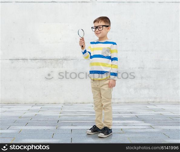 childhood, education, investigation, discovery and people concept - happy little boy in eyeglasses with magnifying glass over urban concrete background