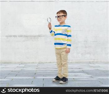 childhood, education, investigation, discovery and people concept - happy little boy in eyeglasses with magnifying glass over urban concrete background