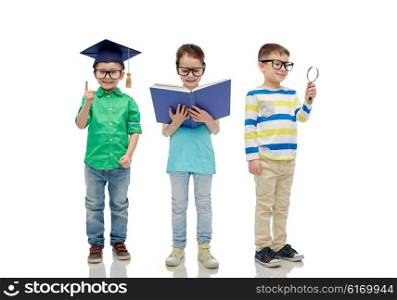 childhood, education, knowledge and people concept - happy little children in eyeglasses with book, magnifying glass and mortar board