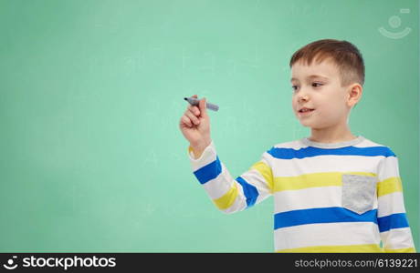 childhood, education, learning and people concept - happy little girl drawing or writing something with marker over green school chalk board background