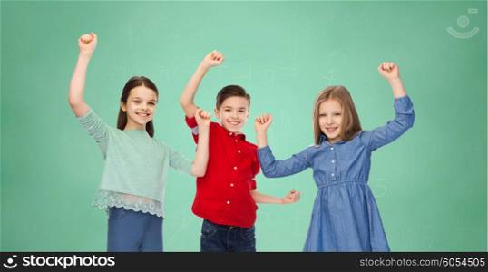 childhood, education, success, gesture and people concept - happy smiling boy and girls raising fists and celebrating victory over green school chalk board background