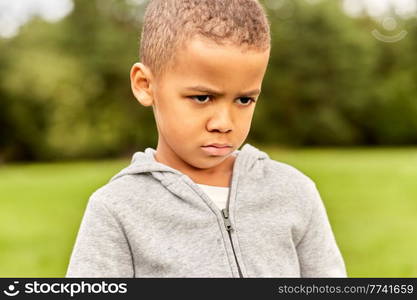 childhood, emotion and people concept - portrait of unhappy little boy at park. portrait of unhappy little boy at park