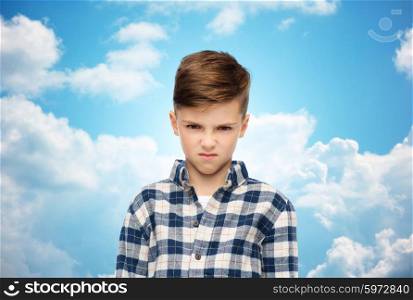 childhood, emotion, anger, hate and people concept - angry boy in checkered shirt over blue sky and clouds background